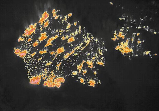 An infrared scan image of a wildfire, of the kind interpreted to map a fire overnight. Against a near-black background, ragged clusters of orange, yellow and white mark heat picked up by the infrared sensor, scattered in patches and streaks across the burned area rather than forming one solid flame front.